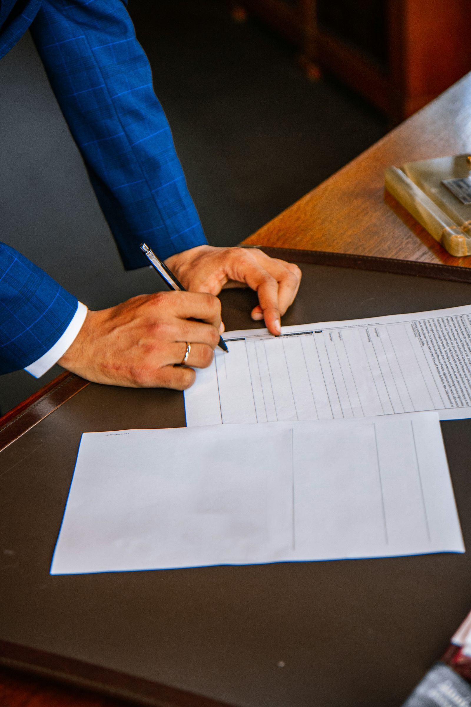 Hands signing a printed form with a pen on a wooden desk